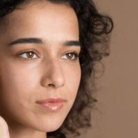 A young caucasian woman with black curly hair touching her face